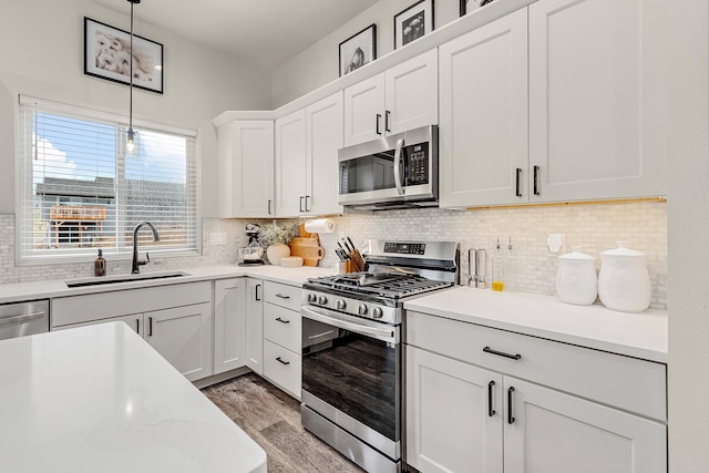 kitchen featuring white cabinetry, appliances with stainless steel finishes, backsplash, hanging light fixtures, and sink