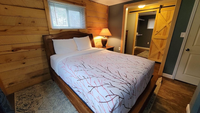 bedroom featuring wood walls, a barn door, and dark hardwood / wood-style flooring