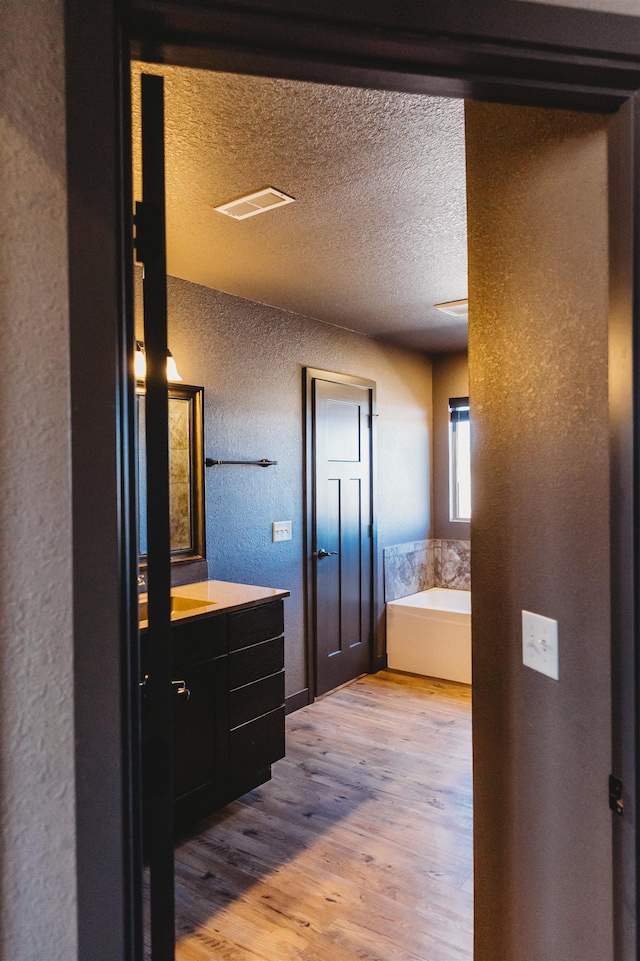 bathroom with hardwood / wood-style floors, a bath, a textured ceiling, and vanity