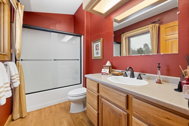 full bathroom with bath / shower combo with glass door, hardwood / wood-style floors, vanity, and toilet