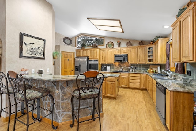 kitchen featuring sink, light wood-type flooring, a kitchen breakfast bar, light stone countertops, and black appliances