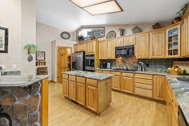 kitchen with black appliances, a kitchen island, light stone countertops, light hardwood / wood-style floors, and backsplash