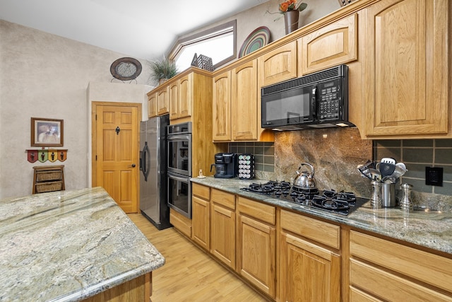 kitchen featuring light stone countertops, backsplash, light hardwood / wood-style flooring, and black appliances