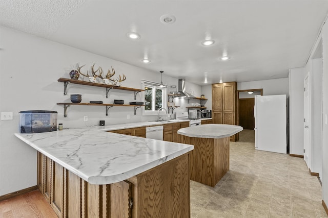 kitchen with pendant lighting, wall chimney range hood, white appliances, a center island, and kitchen peninsula