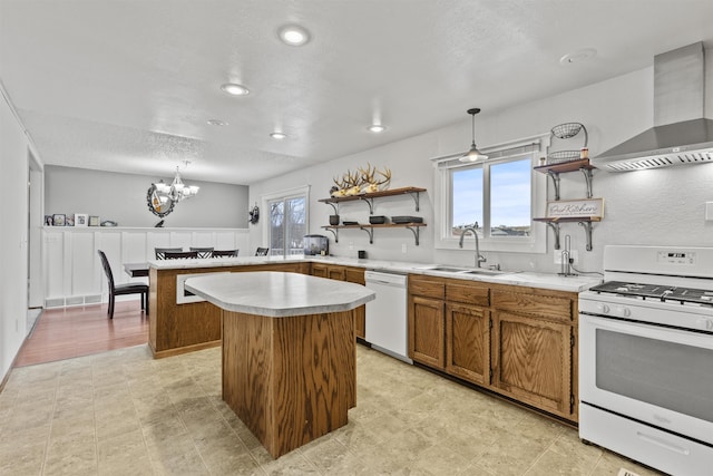 kitchen featuring pendant lighting, sink, white appliances, a kitchen island, and wall chimney exhaust hood