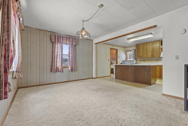 kitchen featuring pendant lighting, light carpet, kitchen peninsula, and wood walls