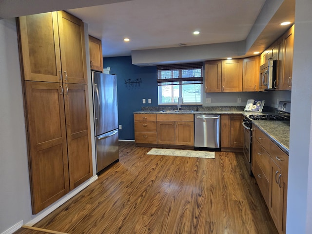 kitchen featuring stainless steel appliances, dark hardwood / wood-style floors, sink, and dark stone counters