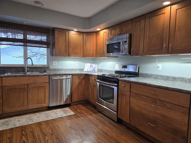 kitchen with appliances with stainless steel finishes, sink, dark stone countertops, and dark hardwood / wood-style flooring