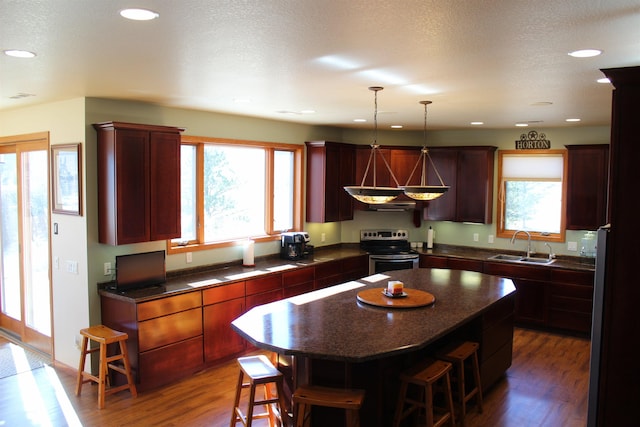 kitchen with a sink, a kitchen breakfast bar, stainless steel electric stove, and dark countertops