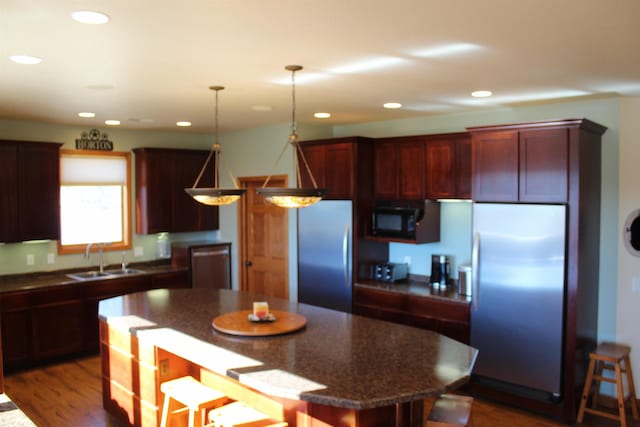 kitchen with a sink, decorative light fixtures, a kitchen breakfast bar, a kitchen island, and appliances with stainless steel finishes