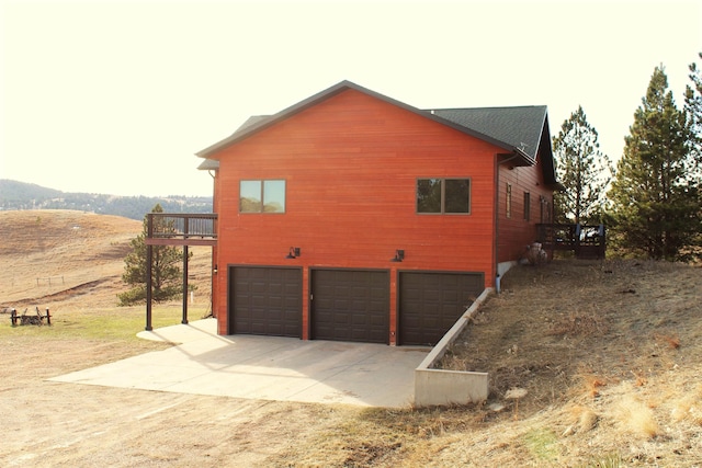 view of side of property featuring a wooden deck, concrete driveway, and an attached garage