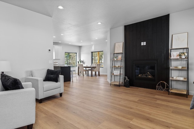 living room with a large fireplace, light hardwood / wood-style floors, and a textured ceiling