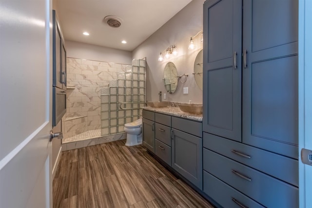 bathroom featuring hardwood / wood-style flooring, tiled shower, vanity, and toilet