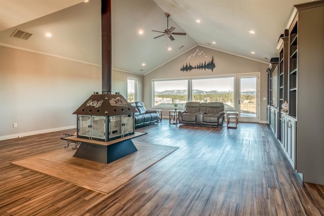 living room with lofted ceiling, ceiling fan, dark hardwood / wood-style floors, ornamental molding, and a wood stove