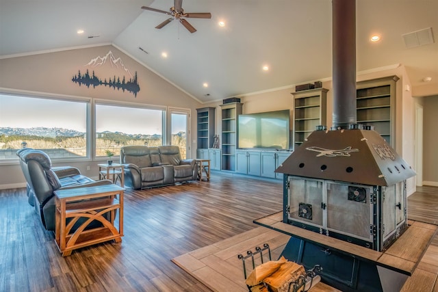 living room featuring vaulted ceiling, wood-type flooring, a wood stove, ornamental molding, and a mountain view