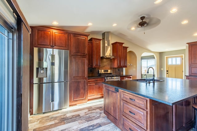 kitchen featuring vaulted ceiling, appliances with stainless steel finishes, sink, wall chimney range hood, and a center island with sink