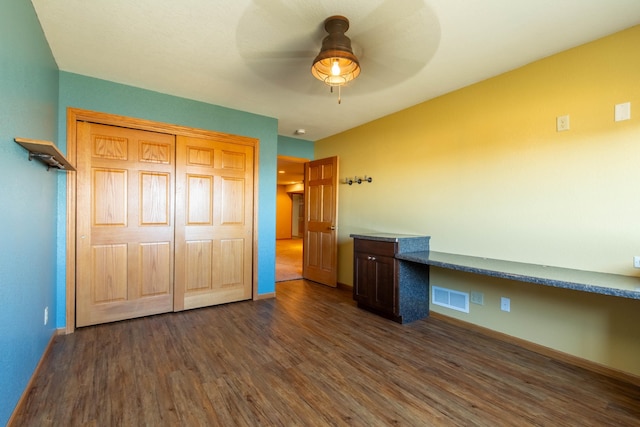 unfurnished bedroom featuring ceiling fan, dark hardwood / wood-style floors, built in desk, and a closet