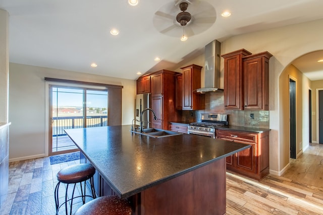 kitchen with appliances with stainless steel finishes, lofted ceiling, sink, a center island with sink, and wall chimney exhaust hood