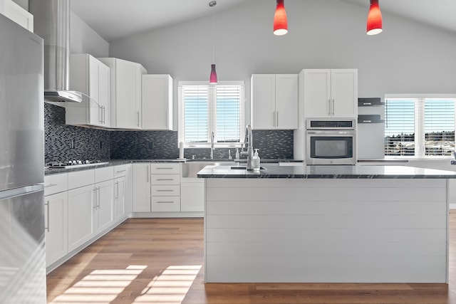 kitchen with white cabinetry, hanging light fixtures, a center island, stainless steel appliances, and light hardwood / wood-style flooring