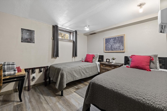 bedroom with hardwood / wood-style flooring, an AC wall unit, and a textured ceiling