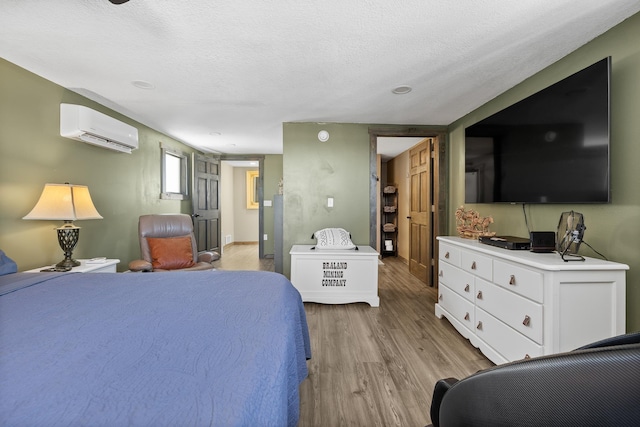 bedroom featuring a wall mounted air conditioner, a textured ceiling, and light wood-type flooring