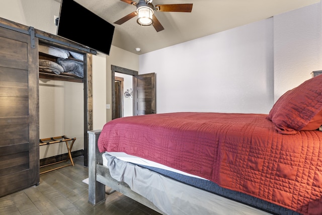 bedroom featuring ceiling fan, a barn door, and dark hardwood / wood-style flooring