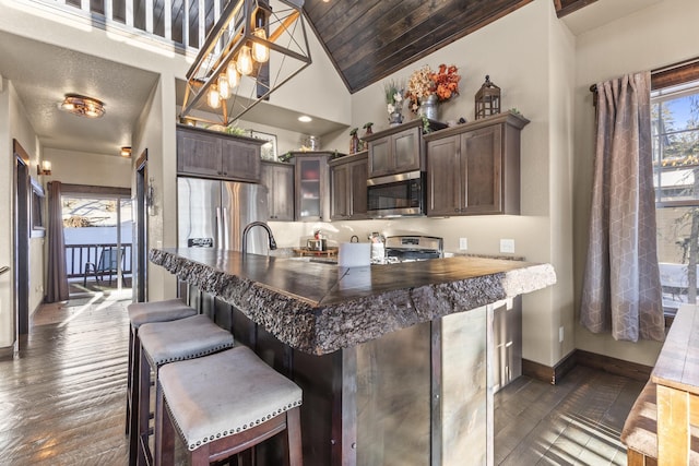 kitchen with a breakfast bar area, appliances with stainless steel finishes, dark brown cabinets, dark hardwood / wood-style flooring, and kitchen peninsula