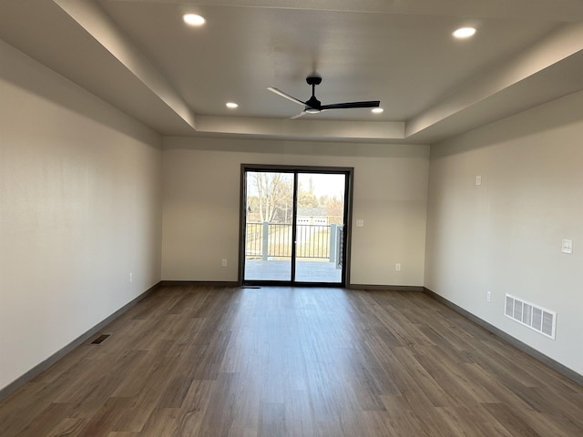 empty room with dark wood-type flooring, ceiling fan, and a tray ceiling