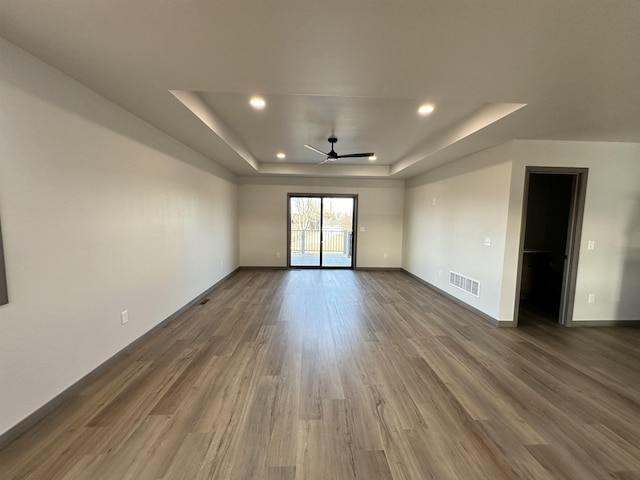 unfurnished room with hardwood / wood-style floors, a raised ceiling, and ceiling fan