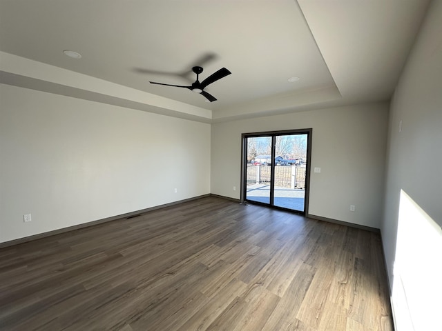 unfurnished room featuring ceiling fan, dark hardwood / wood-style flooring, and a tray ceiling