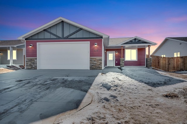 view of front of home featuring an attached garage, stone siding, fence, and board and batten siding