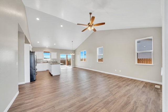 unfurnished living room with light wood-style flooring, baseboards, a sink, and ceiling fan with notable chandelier