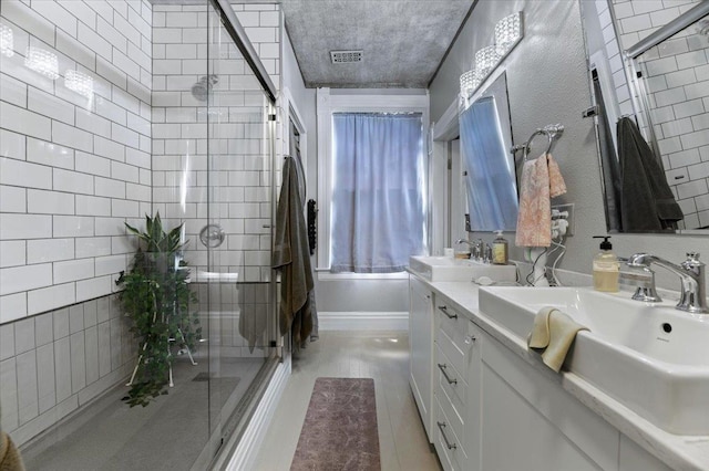 bathroom featuring vanity, a textured ceiling, and combined bath / shower with glass door