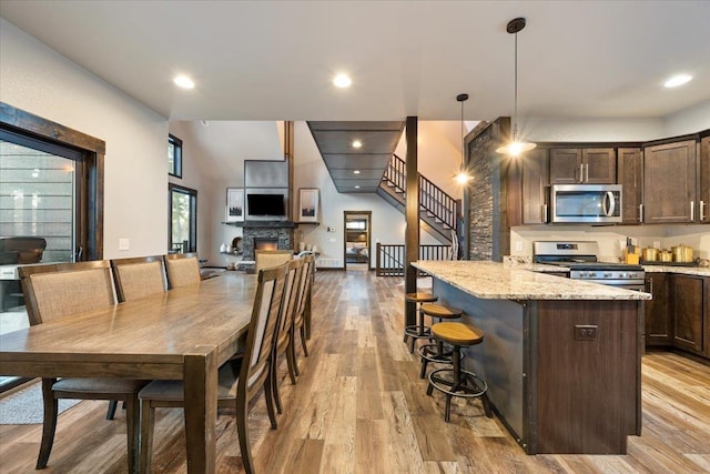 kitchen featuring pendant lighting, stainless steel appliances, a kitchen breakfast bar, light stone counters, and dark brown cabinetry