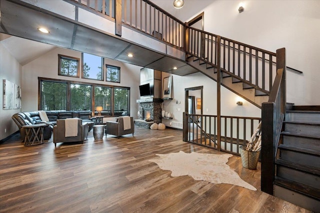 living room featuring hardwood / wood-style flooring, a stone fireplace, and a towering ceiling