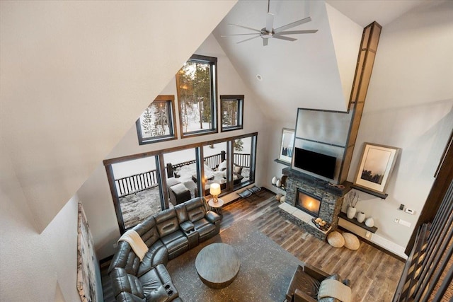 living room featuring hardwood / wood-style floors, a stone fireplace, high vaulted ceiling, and ceiling fan