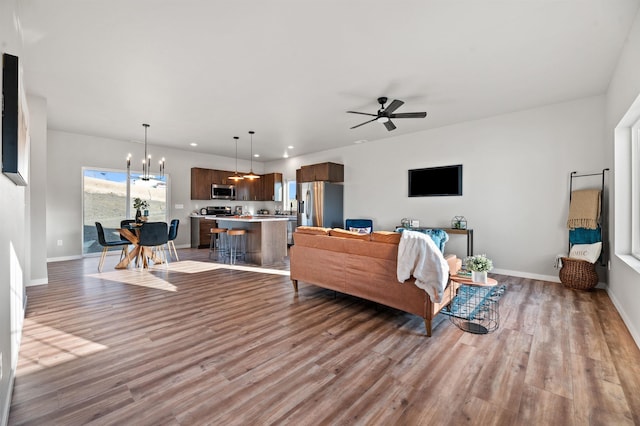 living room featuring ceiling fan with notable chandelier and light hardwood / wood-style flooring