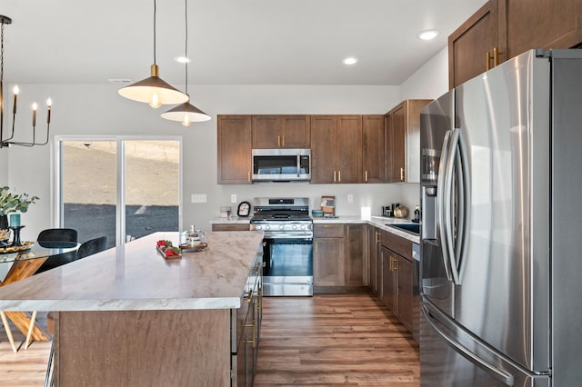 kitchen with hanging light fixtures, a kitchen island, appliances with stainless steel finishes, and dark hardwood / wood-style flooring