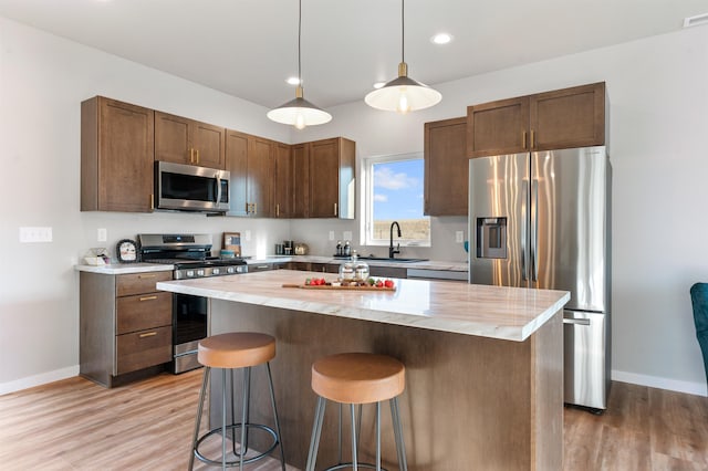 kitchen featuring sink, hanging light fixtures, stainless steel appliances, a kitchen island, and wood counters