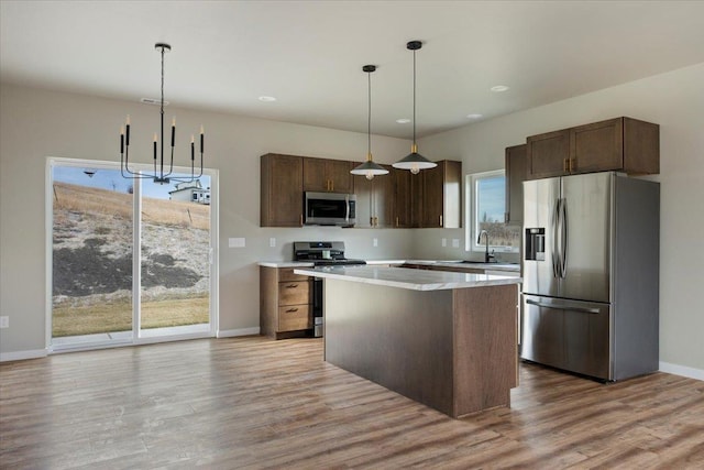 kitchen with pendant lighting, appliances with stainless steel finishes, dark brown cabinetry, a kitchen island, and light wood-type flooring