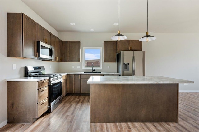 kitchen with sink, appliances with stainless steel finishes, hanging light fixtures, dark brown cabinets, and light hardwood / wood-style floors