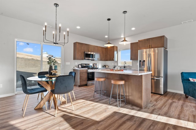 kitchen with stainless steel appliances, a center island, light hardwood / wood-style flooring, and decorative light fixtures