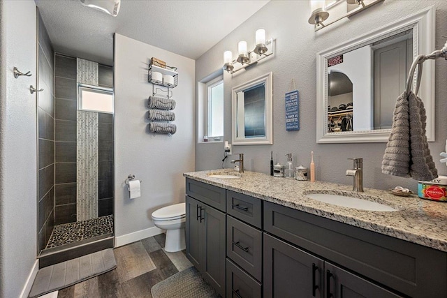 bathroom featuring vanity, a tile shower, wood-type flooring, a textured ceiling, and toilet