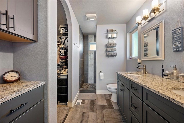 bathroom featuring wood-type flooring, toilet, vanity, and a tile shower