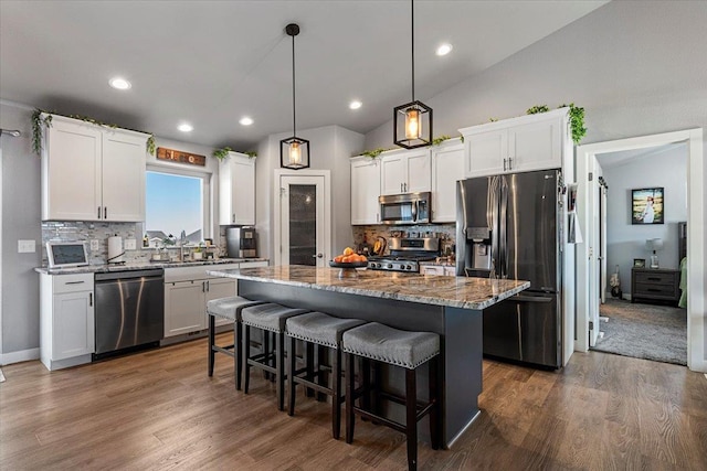 kitchen featuring stone counters, a kitchen island, decorative light fixtures, white cabinetry, and stainless steel appliances