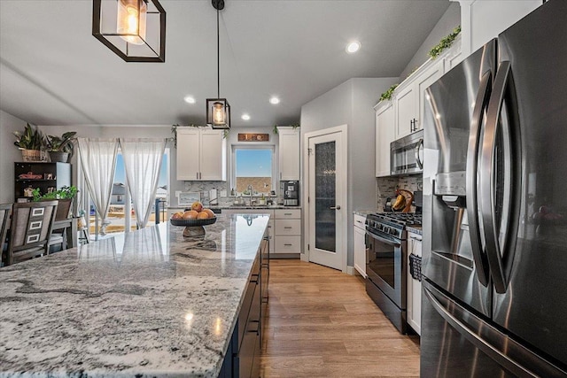 kitchen with decorative light fixtures, a kitchen island, stainless steel appliances, light stone countertops, and white cabinets