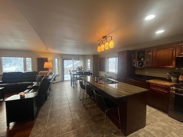 kitchen with a kitchen breakfast bar, sink, a center island with sink, and stainless steel gas stove