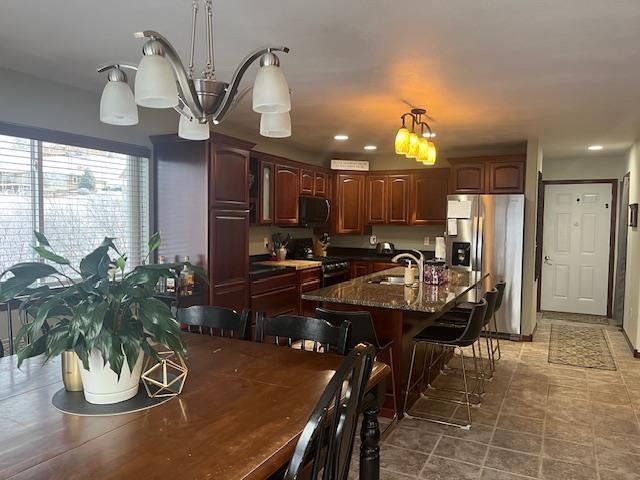 kitchen featuring sink, a kitchen bar, stove, a kitchen island with sink, and stainless steel fridge with ice dispenser