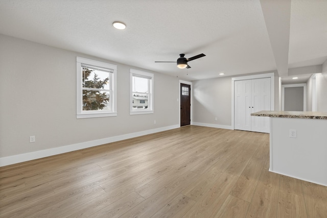 unfurnished living room featuring a textured ceiling, ceiling fan, and light hardwood / wood-style flooring