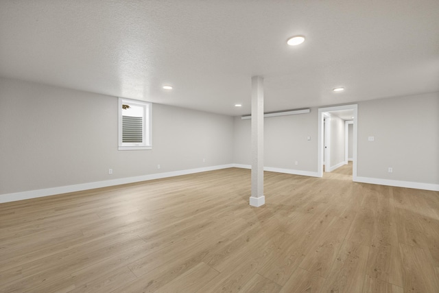 basement featuring light wood-type flooring and a textured ceiling